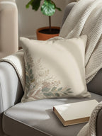 Cream throw pillow with muted floral and leaf corner design on armchair.