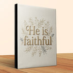 Book with "He is faithful" text and floral design on beige cover.