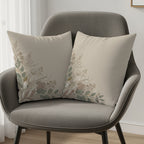Two decorative throw pillows with floral branch design on a gray armchair.