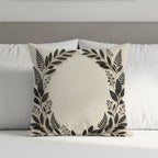 Cream throw pillow with dark leaf wreath design on a bed.
