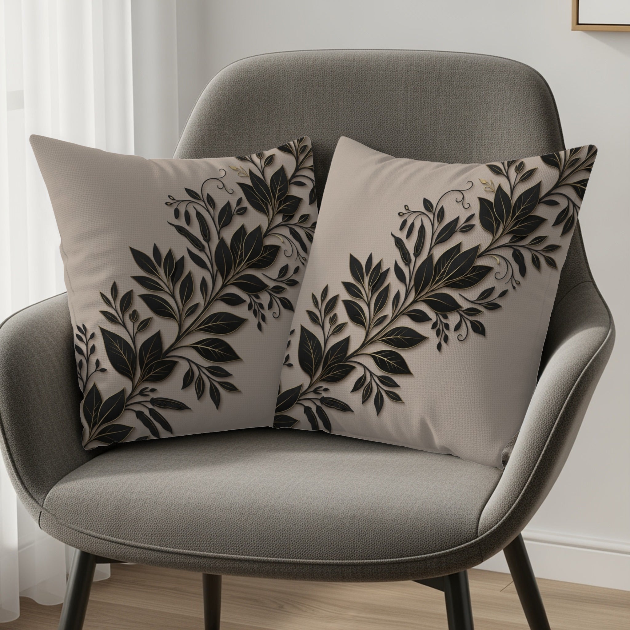 Two beige throw pillows with black floral vine designs on a grey armchair.