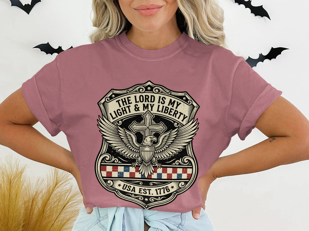 T-shirt with shield graphic featuring a cross, eagle, and text "The Lord is my Light & My Liberty" and "USA Est. 1776".