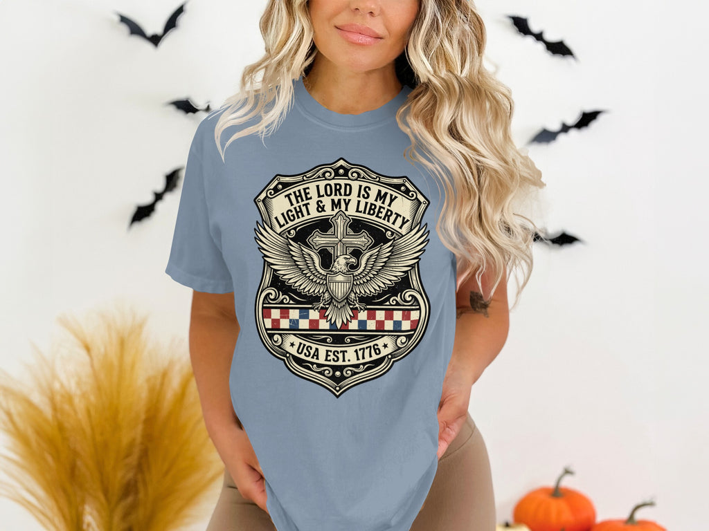 Light blue t-shirt with shield emblem, USA EST 1776, cross, wings, and eagle.