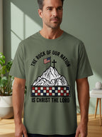 Green t-shirt with mountain, flag, cross, and text: "THE ROCK OF OUR NATION IS CHRIST THE LORD".