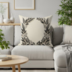 Beige throw pillow with a dark floral wreath design on a sectional sofa.