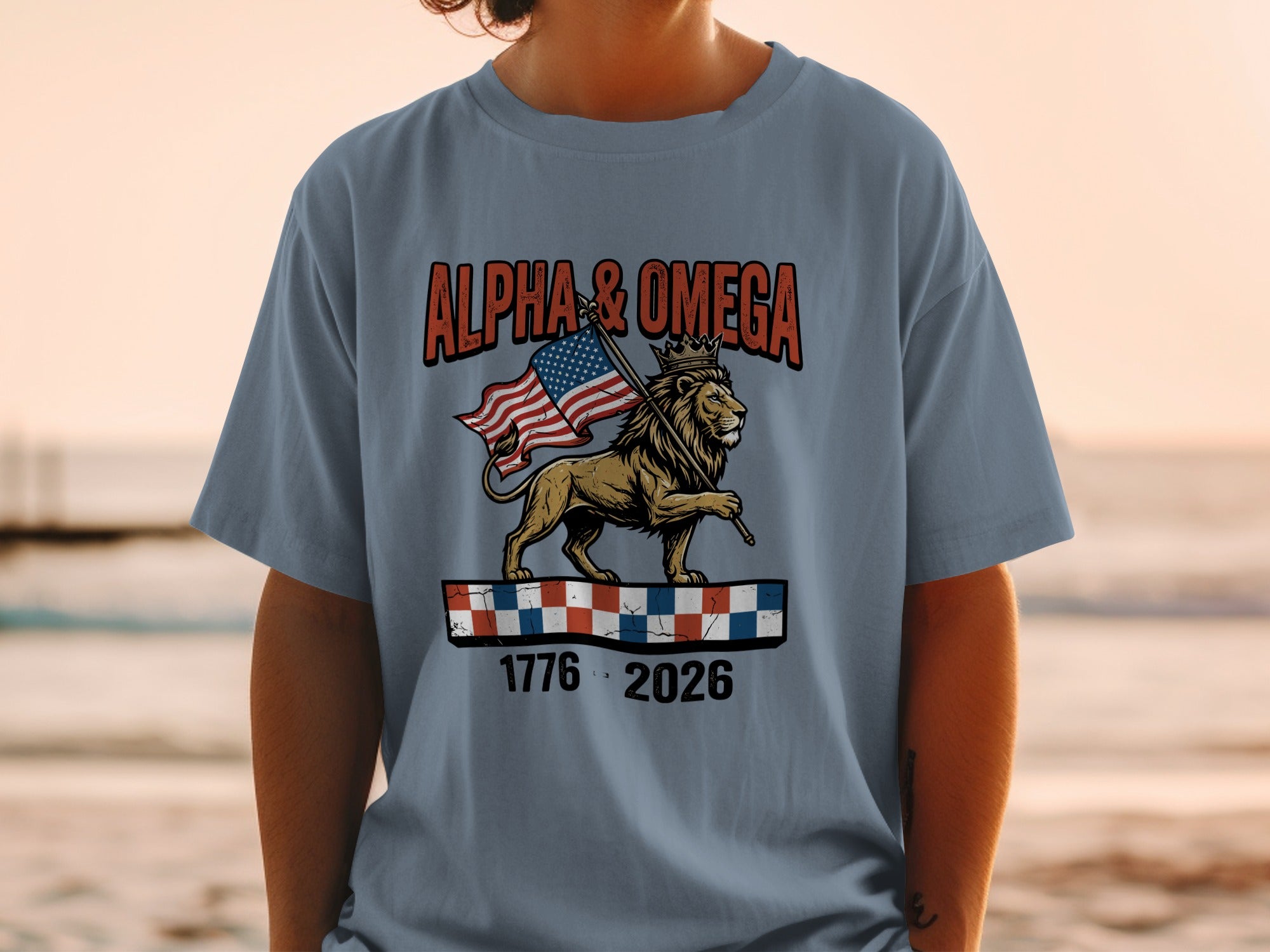 T-shirt with lion holding American flag, text "Alpha & Omega", and dates 1776-2026.