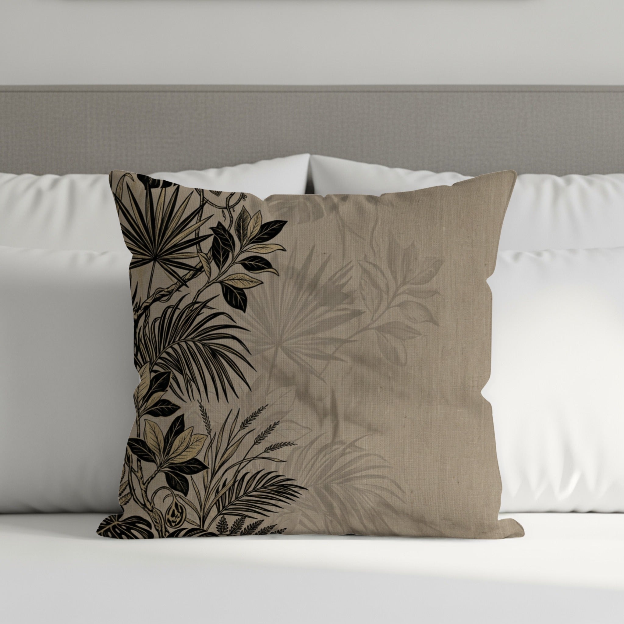 Tan throw pillow with black botanical print on a bed.