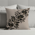 Beige throw pillow with gold leaf vine embroidery on a bed.
