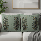 Two sage green throw pillows with gold floral designs on a sofa.