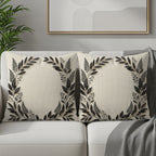 Two square decorative pillows with a dark floral wreath design on a cream background.