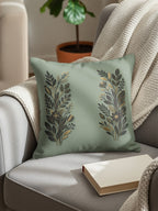 Sage green throw pillow with gold floral motifs on a gray armchair.