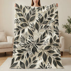 Cream blanket with gold and black botanical leaf pattern and subtle religious symbols.