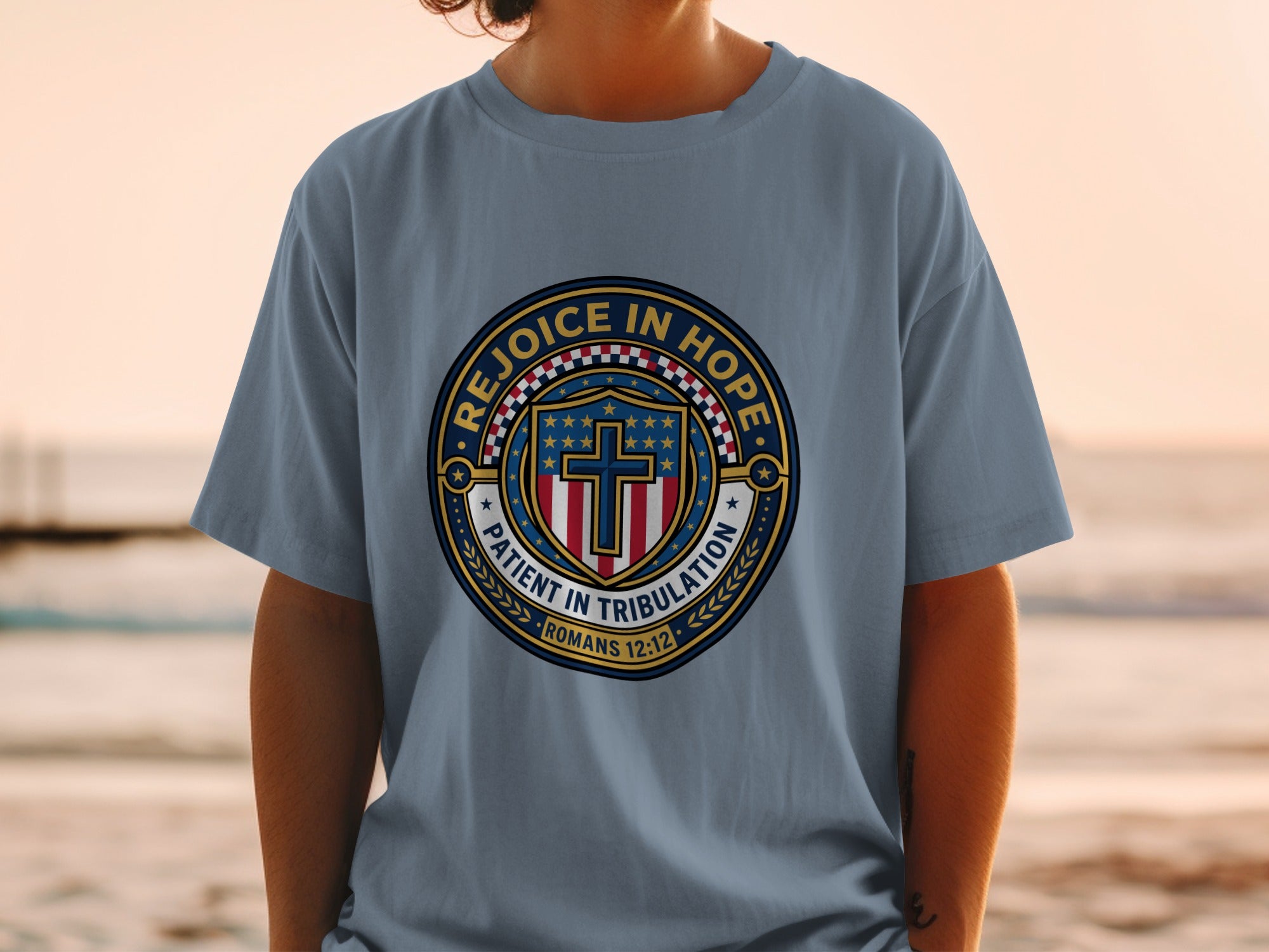 Blue t-shirt with circular emblem featuring "REJOICE IN HOPE" and "PATIENT IN TRIBULATION ROMANS 12:12".