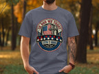 Gray t-shirt with "IN GOD WE TRUST" emblem, featuring a cross, flag, and "1776 2026".