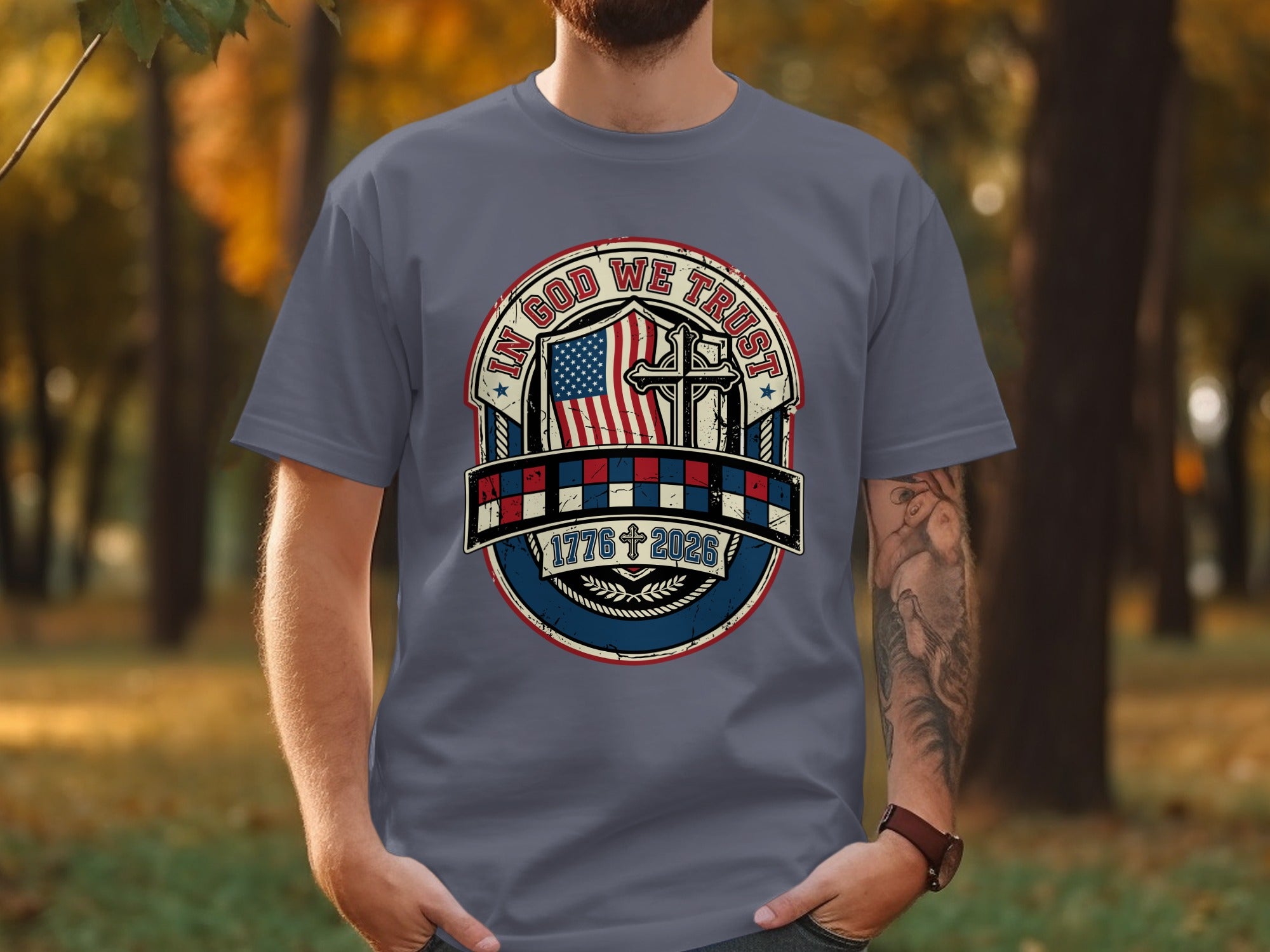 Gray t-shirt with "IN GOD WE TRUST" emblem, featuring a cross, flag, and "1776 2026".
