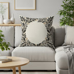 Cream cushion with ornate black and gold floral wreath design on a sofa.