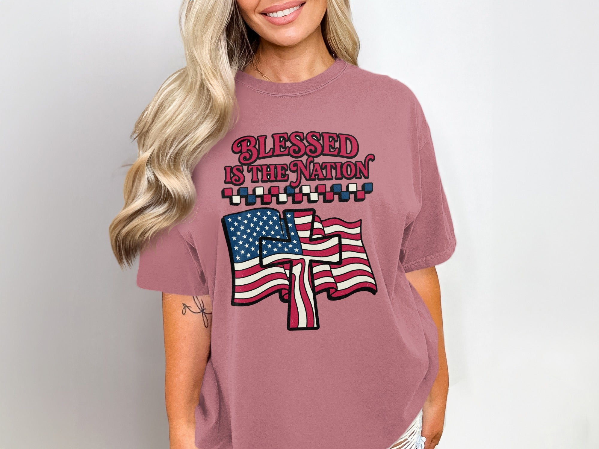 Woman wearing dusty rose t-shirt with "Blessed is the Nation" and US flag graphic.
