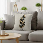 Throw pillow with black and gold metallic leaf design on textured beige fabric.