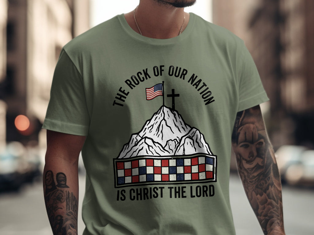 Olive t-shirt with mountain, flag, cross, and text "The Rock of Our Nation is Christ the Lord".
