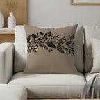 Tan throw pillow with black floral branch design on neutral couch.