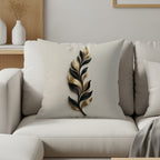 Cream throw pillow with black and gold leaf design on couch.
