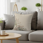 Cream pillow with delicate floral and leafy vine design on gray sofa.