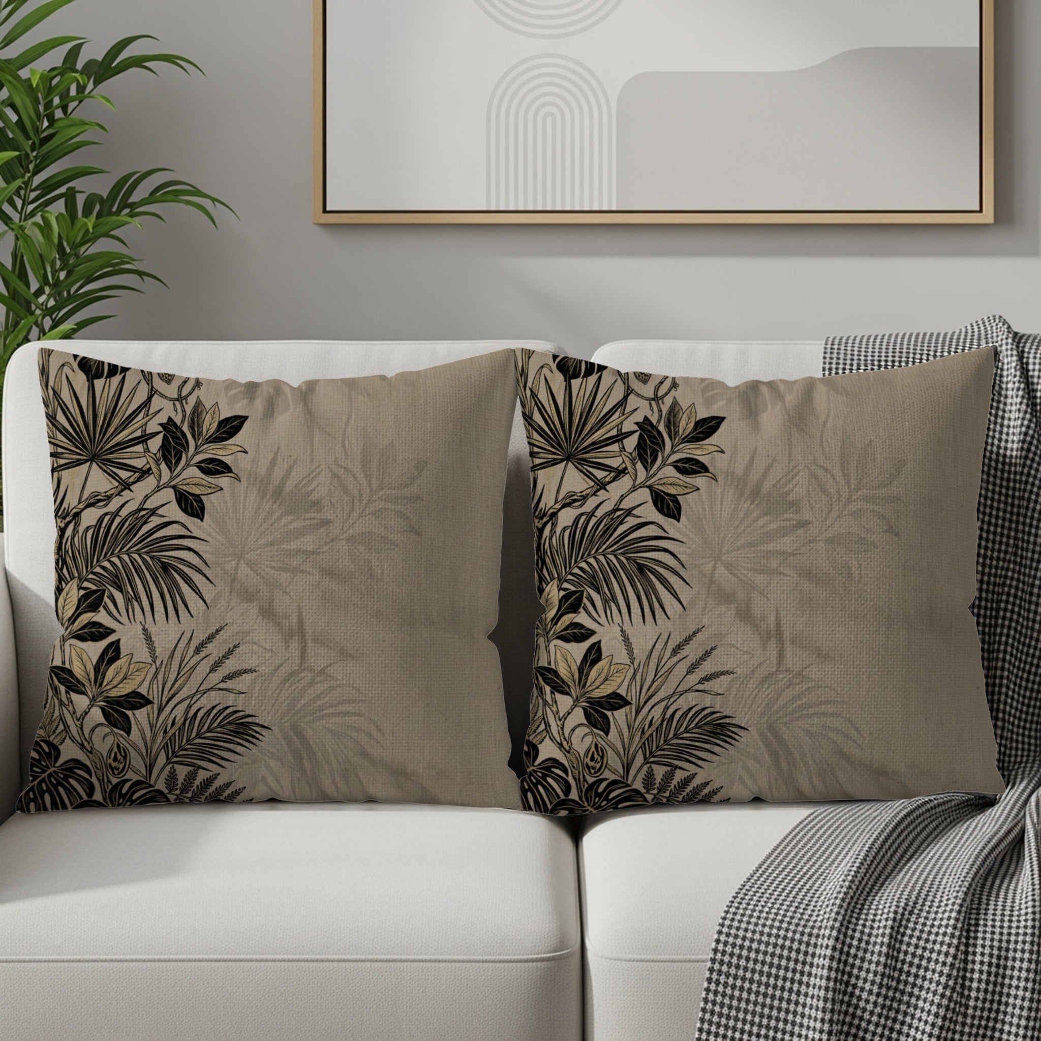 Two neutral throw pillows with dark botanical leaf print on a white sofa.
