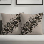 Two beige throw pillows with black and gold floral vine design on a couch.