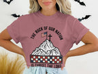 T-shirt with mountain, American flag, cross, and text "The Rock of Our Nation is Christ the Lord".