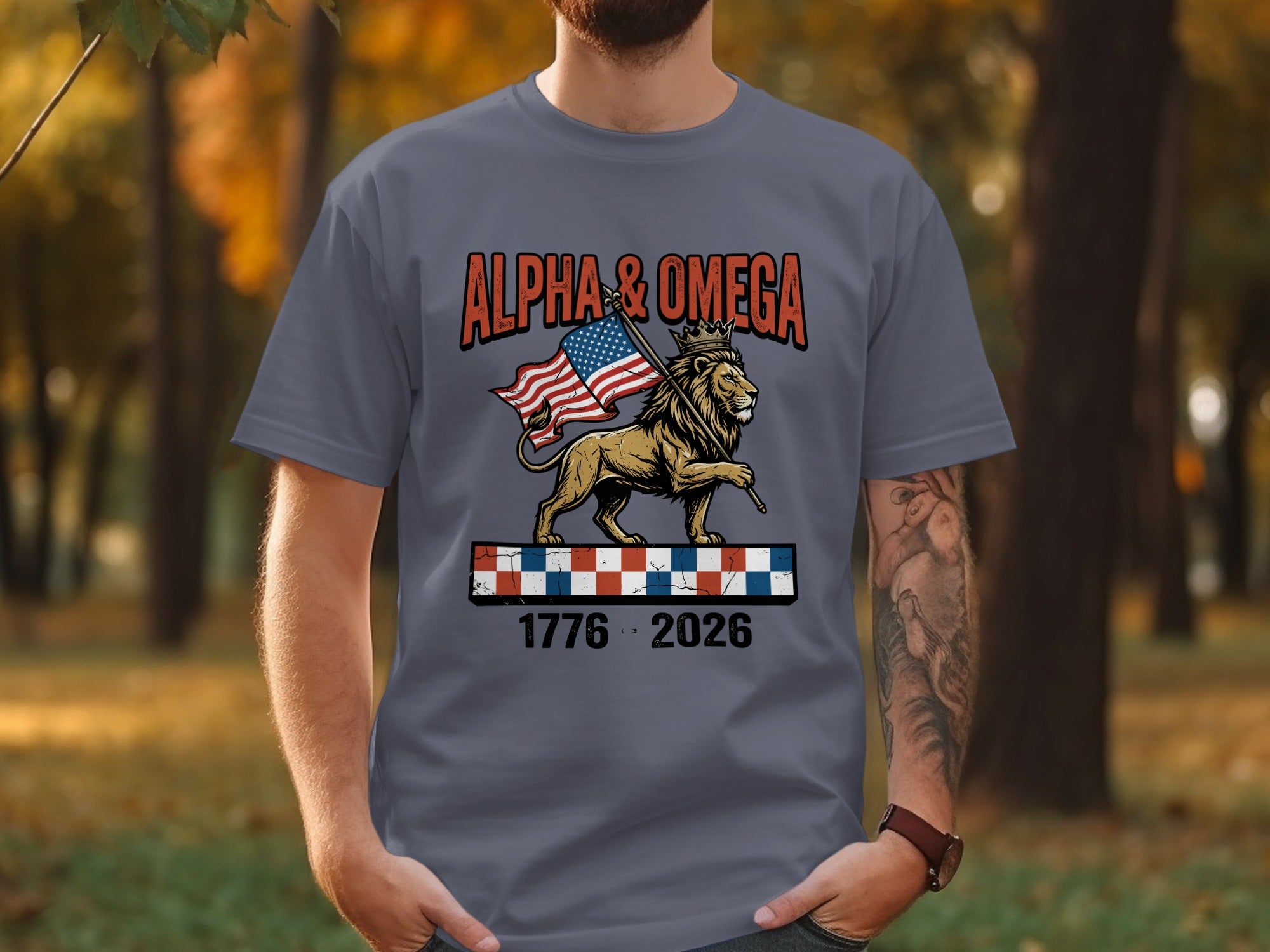 Gray t-shirt with lion, crown, American flag, and text "Alpha & Omega 1776-2026".