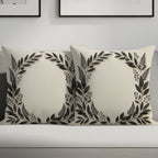 Two cream throw pillows with dark floral leaf wreaths on a couch.