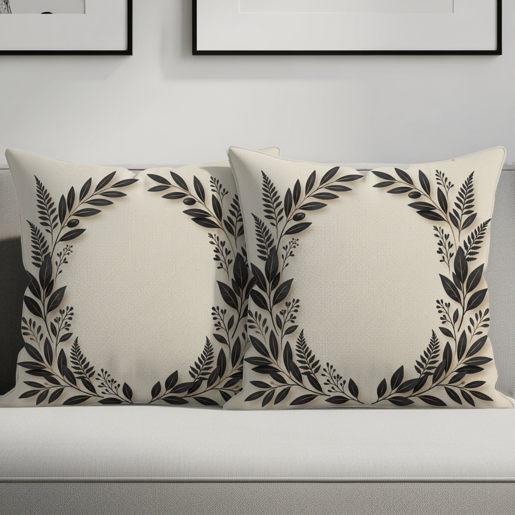 Two cream throw pillows with dark floral leaf wreaths on a couch.