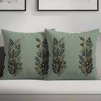 Two sage green throw pillows with botanical gold and black design.
