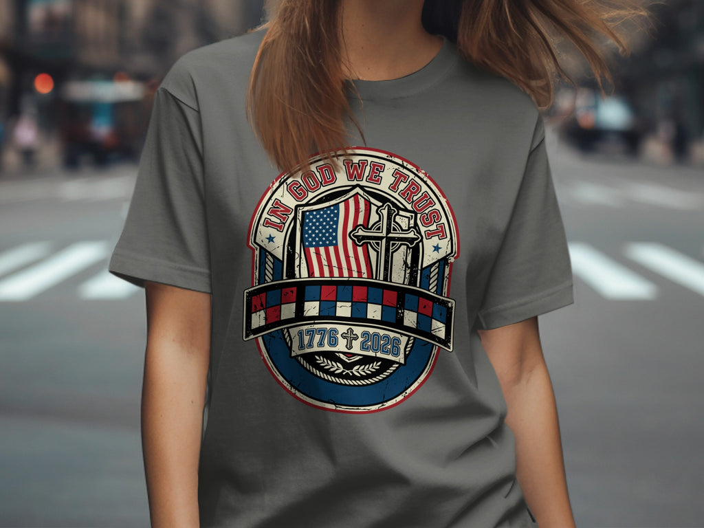 Gray t-shirt with circular patriotic design featuring US flag, cross, and dates 1776-2026.