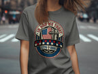 Gray t-shirt with circular patriotic design featuring US flag, cross, and dates 1776-2026.