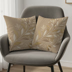 Two beige decorative pillows with a raised floral pattern on a gray armchair.