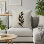 Cream pillow with gold and black abstract feather design on couch.
