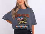 Lion wearing crown holding American flag, with "ALPHA & OMEGA" and "1776 - 2026".