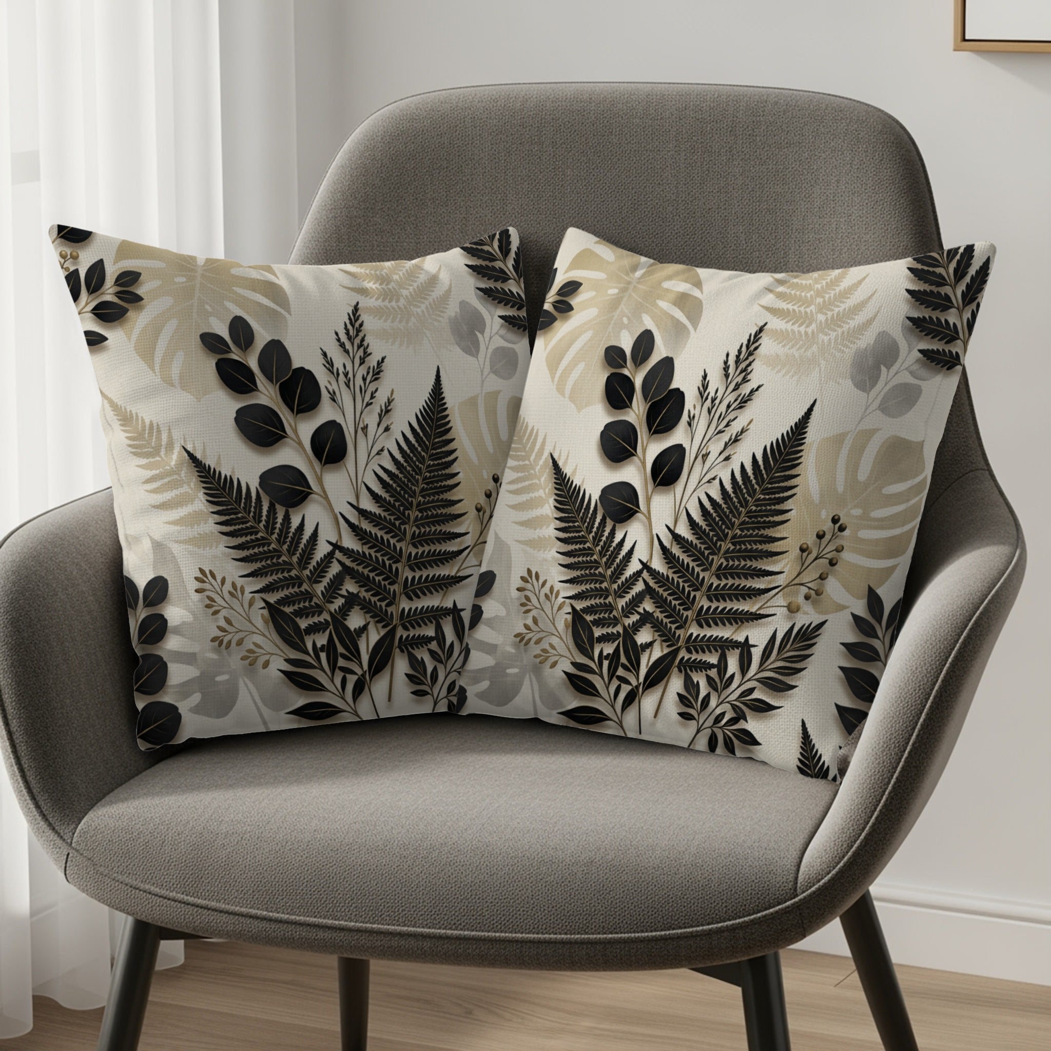 Two decorative throw pillows with black and beige fern and leaf patterns on a grey armchair.