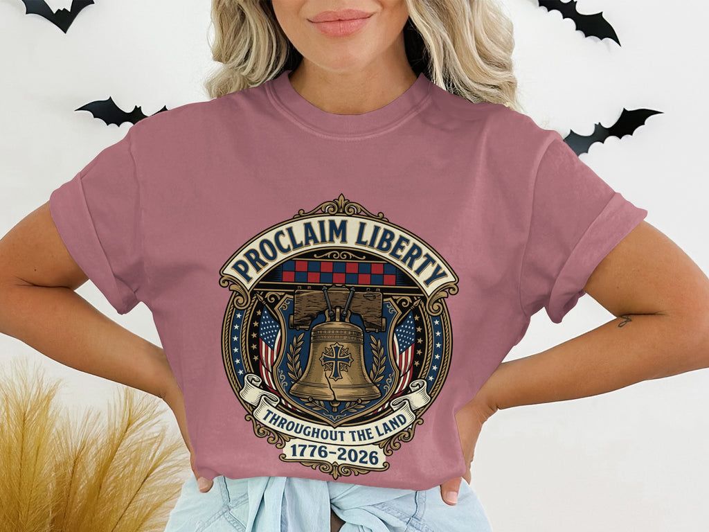 Rose t-shirt with circular emblem depicting Liberty Bell, flags, and "Proclaim Liberty 1776-2026."