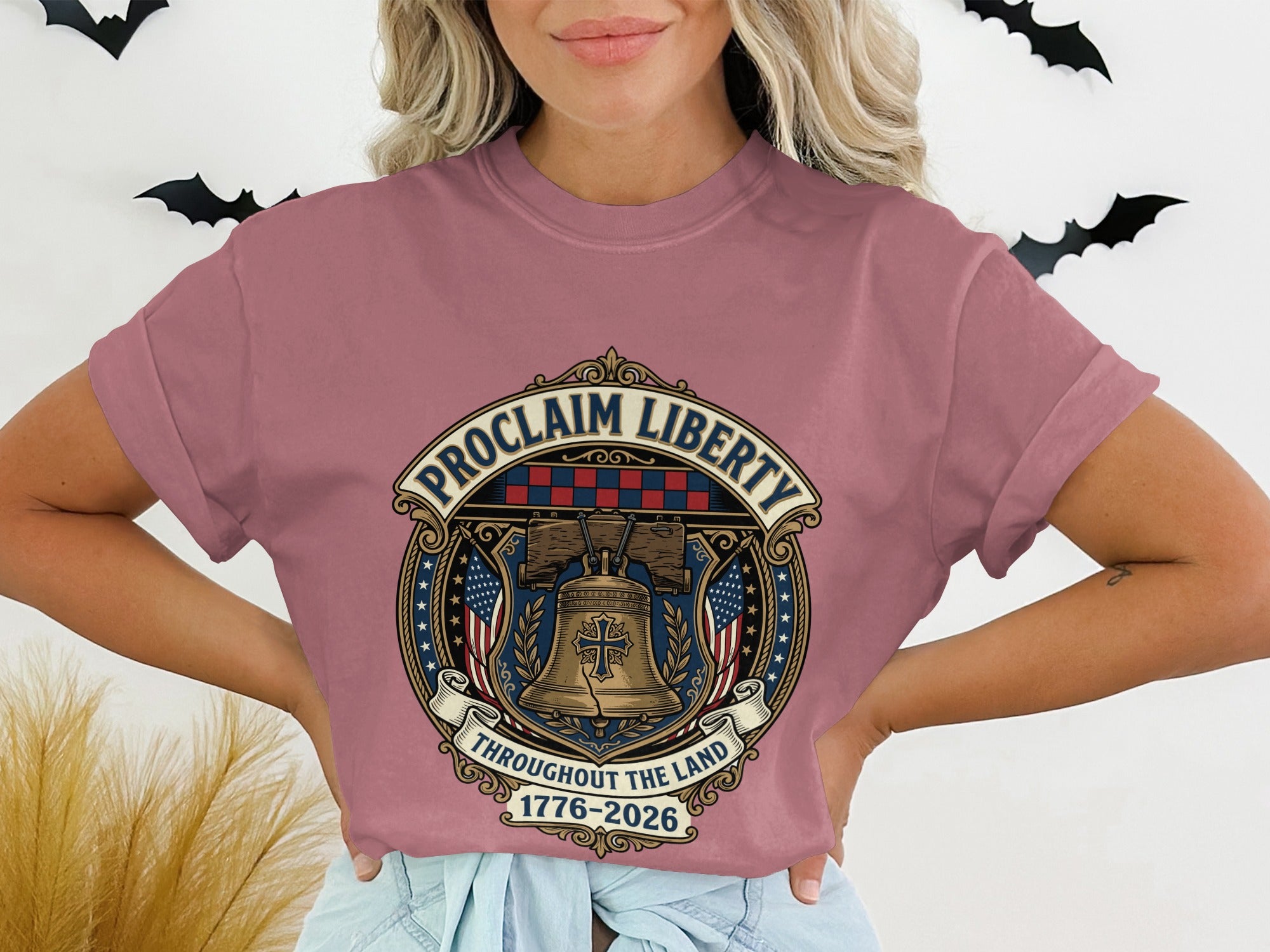 Rose t-shirt with circular emblem depicting Liberty Bell, flags, and "Proclaim Liberty 1776-2026."