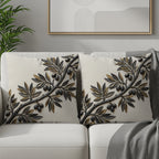 Two cream decorative pillows with embossed olive branch design on a sofa.