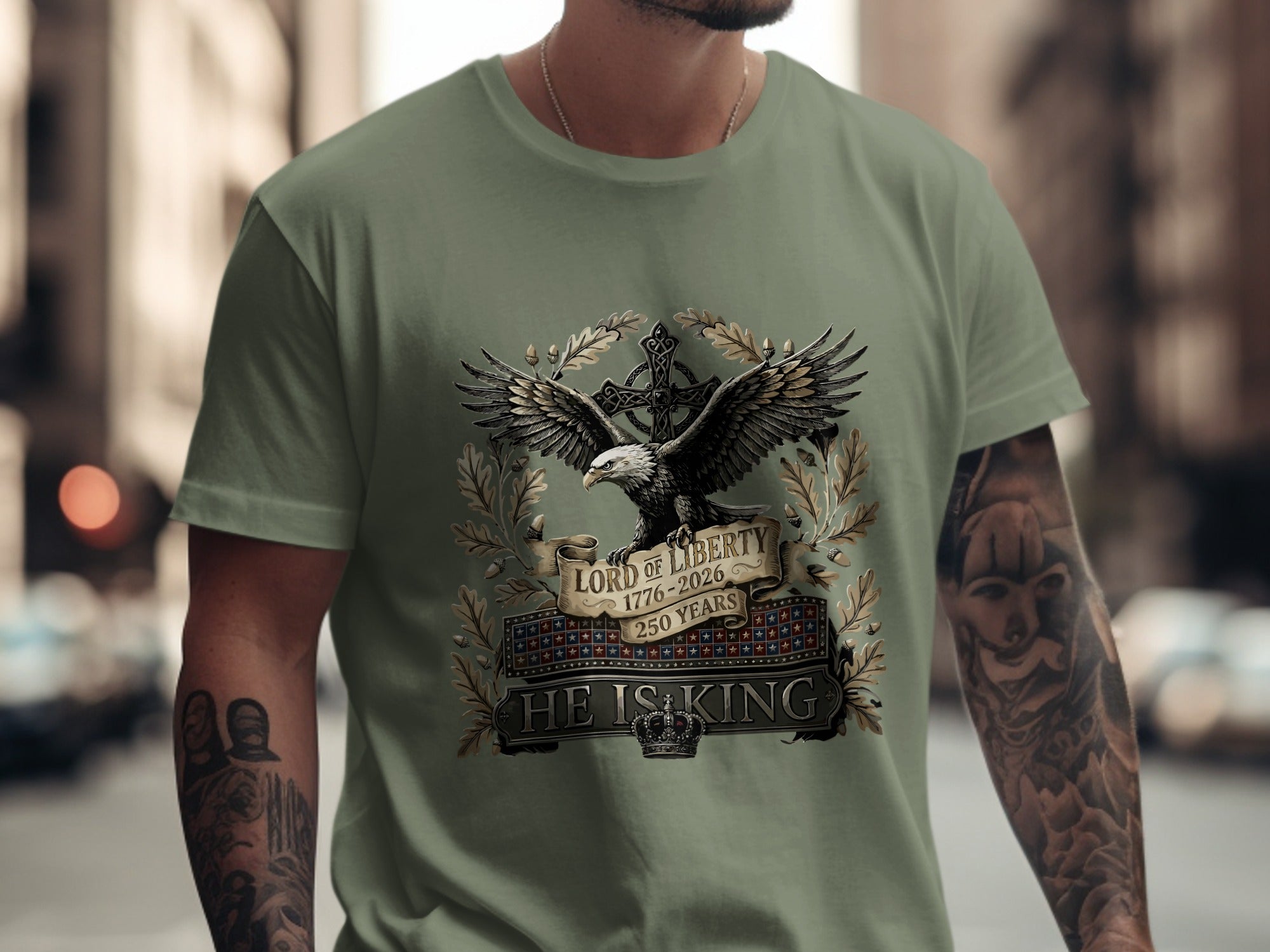 Olive green t-shirt featuring an eagle, cross, and banner reading "Lord of Liberty 1776-2026 HE IS KING".