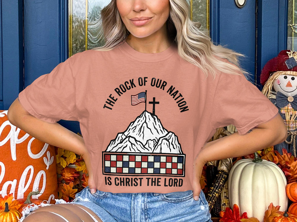 Peach t-shirt with "The Rock of Our Nation Is Christ the Lord" and American flag on mountain.