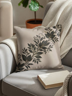 Beige throw pillow with dark floral branch design on armchair.
