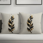 Two cream throw pillows with black and gold feather designs on a sofa.