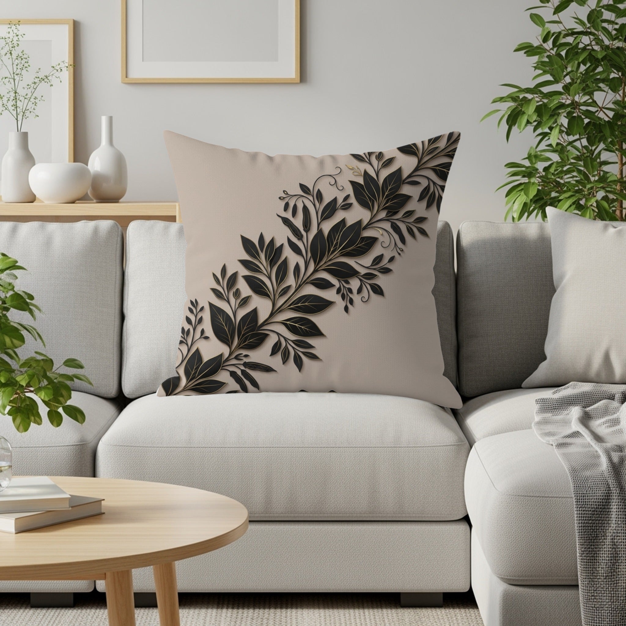 Beige throw pillow with black and gold leaf design on a white sofa.