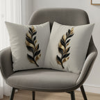 Two decorative throw pillows with black and gold feather motifs on a gray chair.