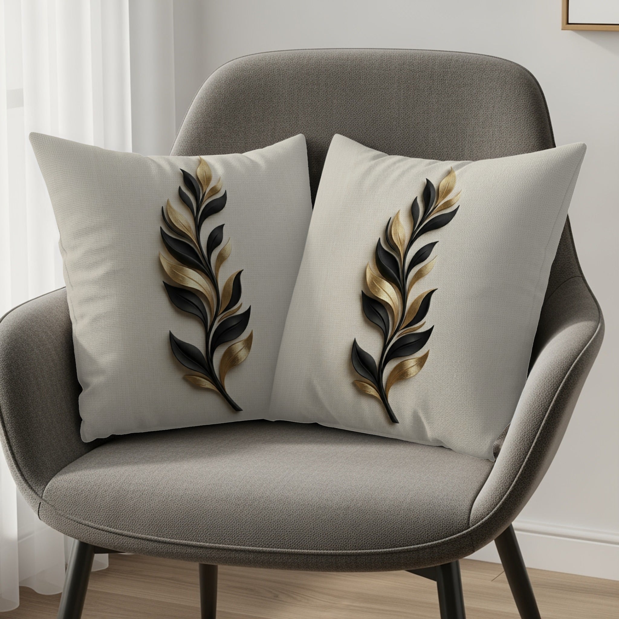 Two decorative throw pillows with black and gold feather motifs on a gray chair.