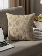 Beige throw pillow with a delicate gold and green leaf pattern on a sofa.